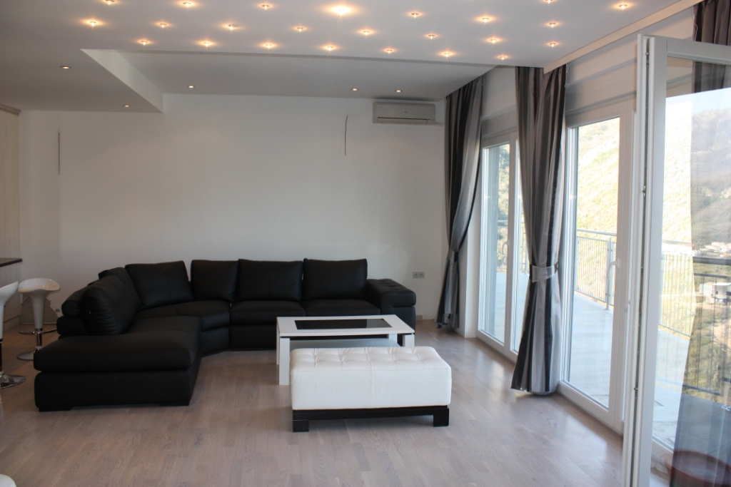 Modern living room with a black leather sofa and panoramic windows in an apartment in Becici, Montenegro.