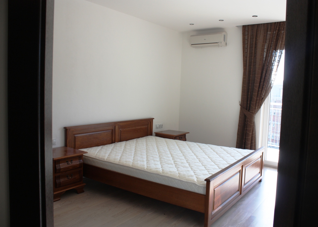 Bright bedroom with a double bed in an apartment, Becici, Montenegro: wooden furniture and access to the balcony.