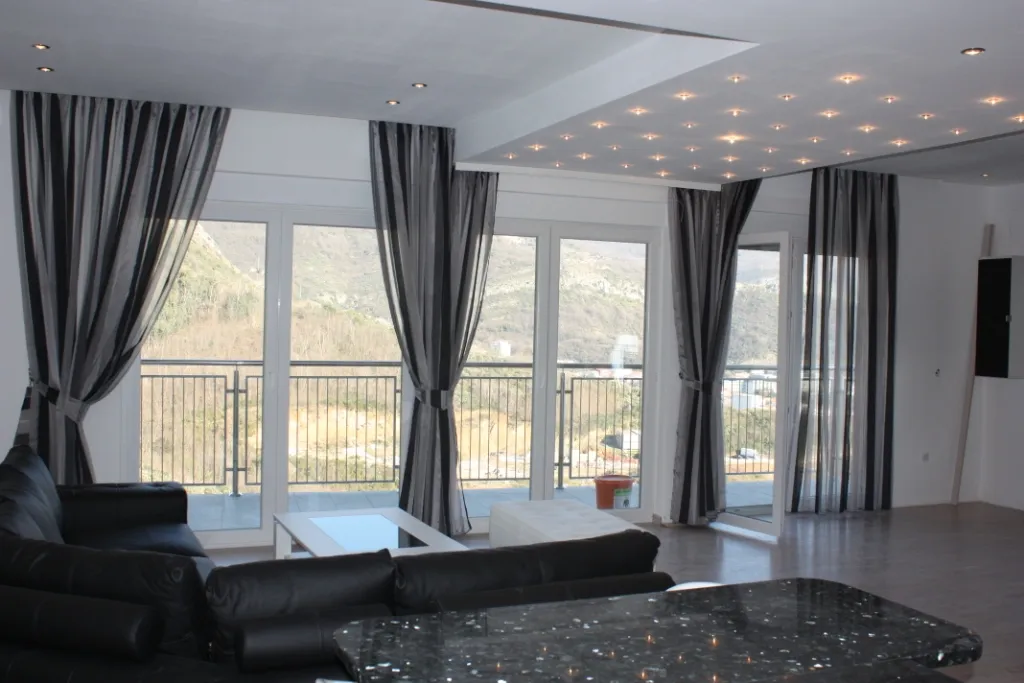 Living room with black leather sofa, marble table, and starry ceiling lights overlooking hills.