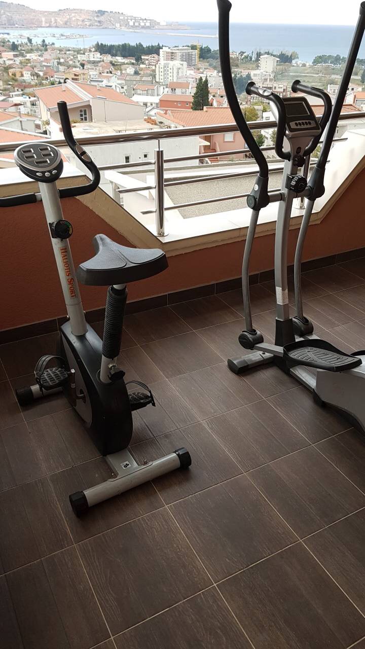 Exercise equipment on the balcony of a house in Shushan, Montenegro, with panoramic views of the sea and cityscape.