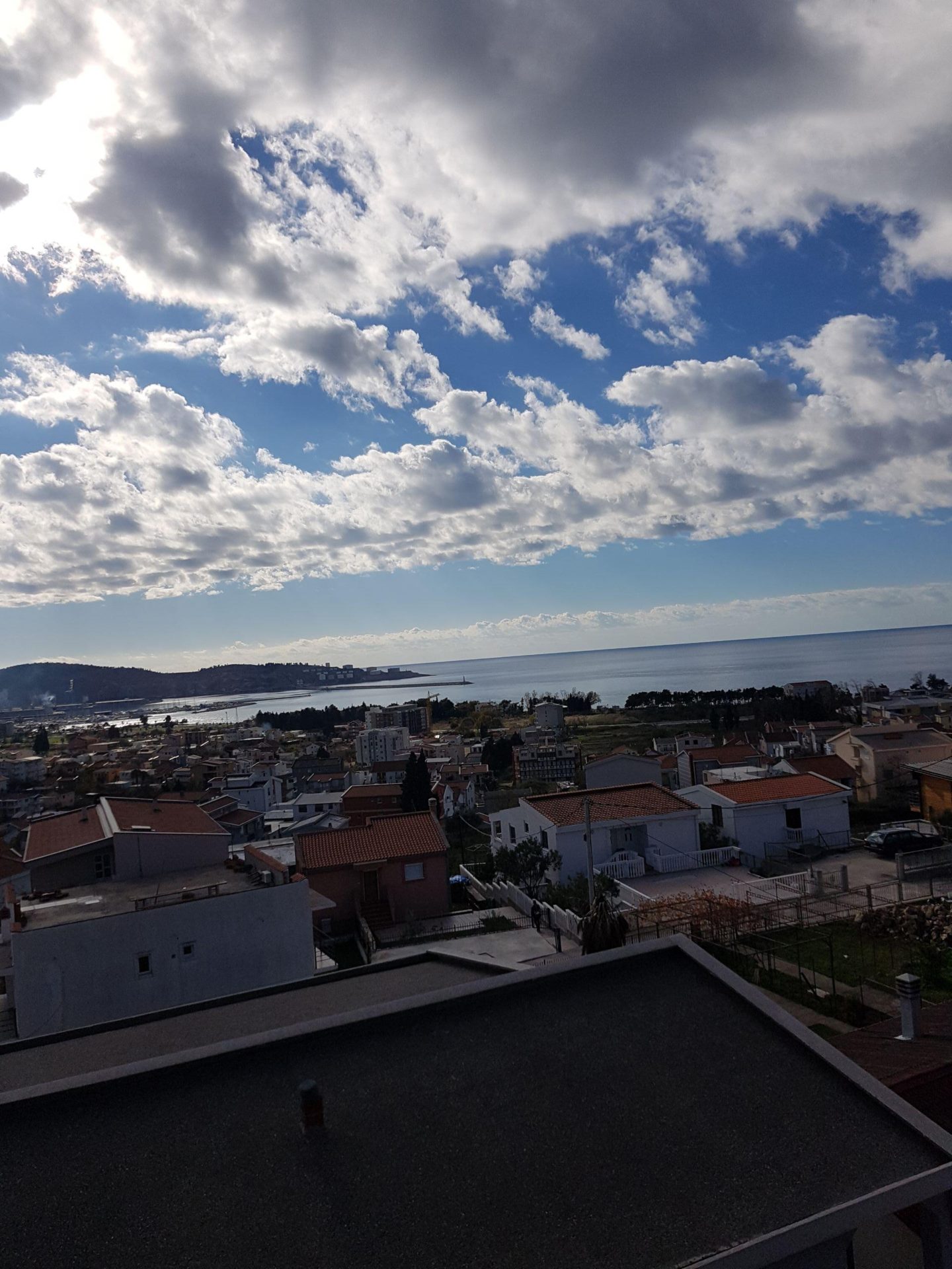 Panoramic view of the sea and the city of Shushan in Montenegro from the roof of the house, with tiled roofs and a coastal landscape visible.