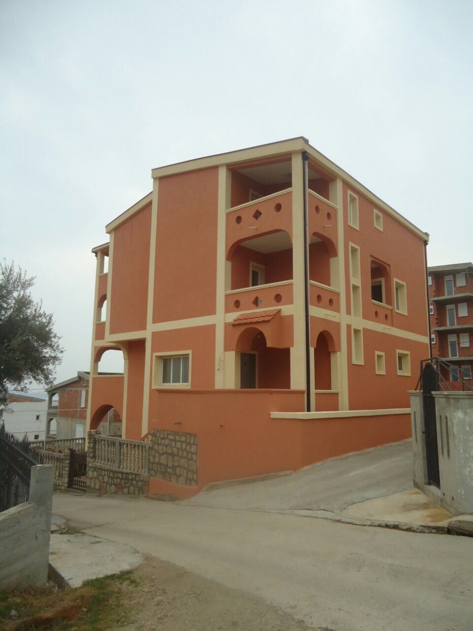 Three-story terracotta-colored house with arched balconies in Šušanj, Montenegro, exterior view.
