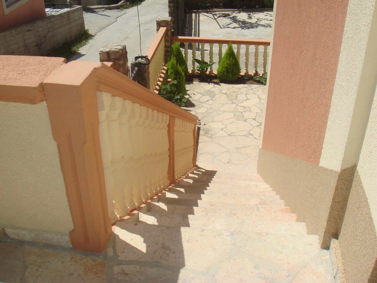 Stone staircase with balustrade by the house in Shushan, Montenegro, overlooking the terrace and landscaped yard with plants.
