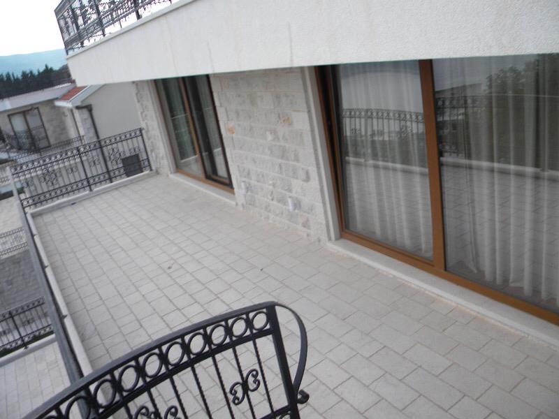 Open terrace with stone pavers and black wrought iron railing attached to a building facade.