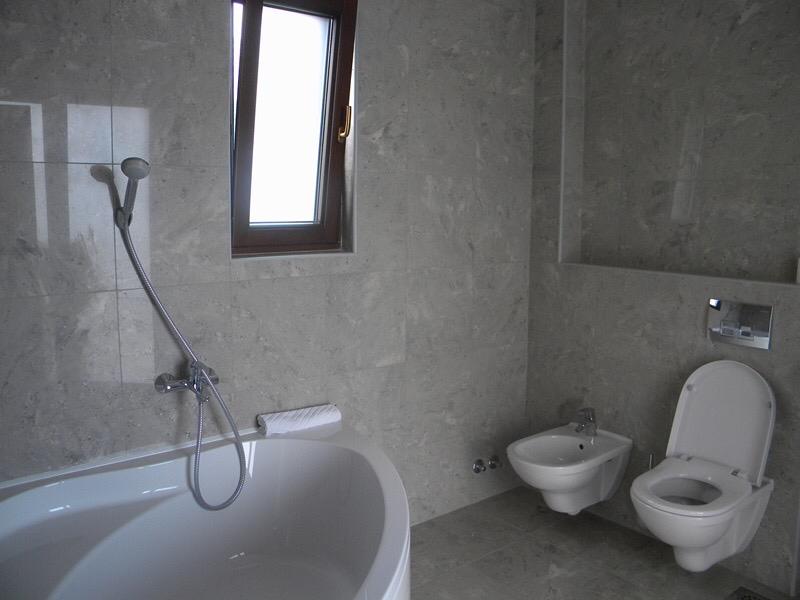 Bathroom featuring a white bathtub, handheld shower, toilet, and bidet on grey stone tiles.