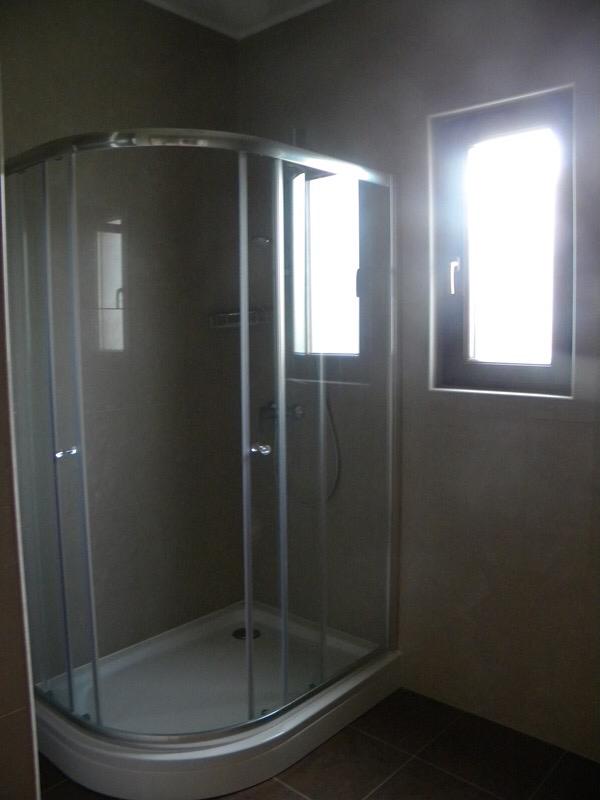 Corner glass shower enclosure with chrome frame and white tray against gray tiled walls.