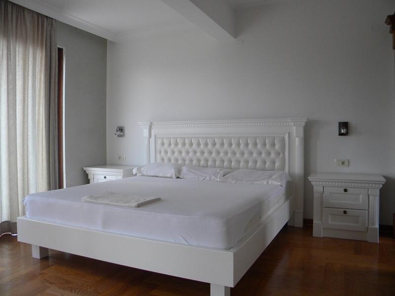 Bedroom with a white double bed and nightstands in a villa in Herceg Novi, Montenegro, parquet flooring, bright interior.
