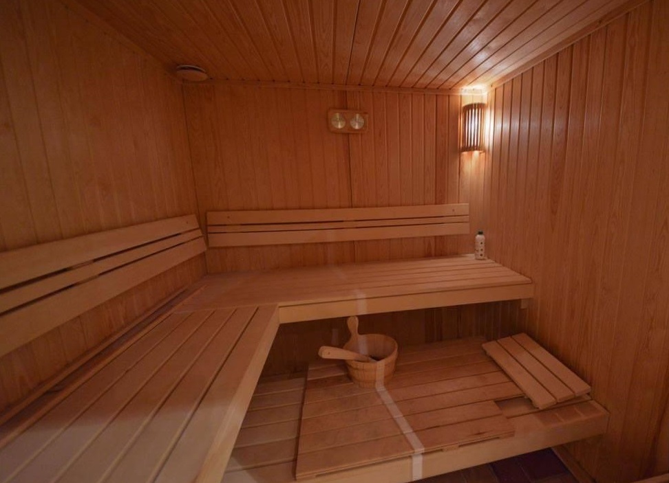 Wooden sauna interior with tiered benches, a bucket, and a ladle on the floor.