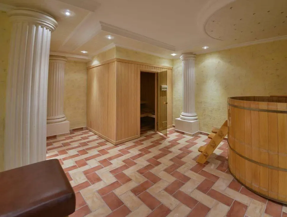 Sauna room with a wooden cabin, large barrel tub, and decorative white columns on tiled floor.