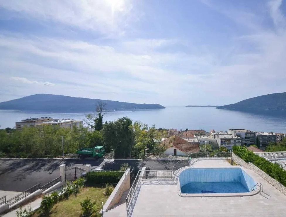 Open pool on a terrace overlooking the sea and mountains. Urban landscape and greenery are visible below.