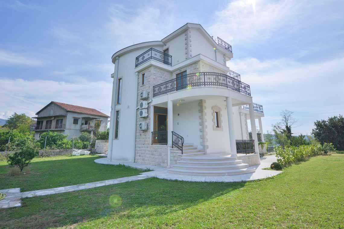 Three-story villa in Herceg Novi, Montenegro: white stone facade, wrought-iron balconies, and a well-kept garden around the house.
