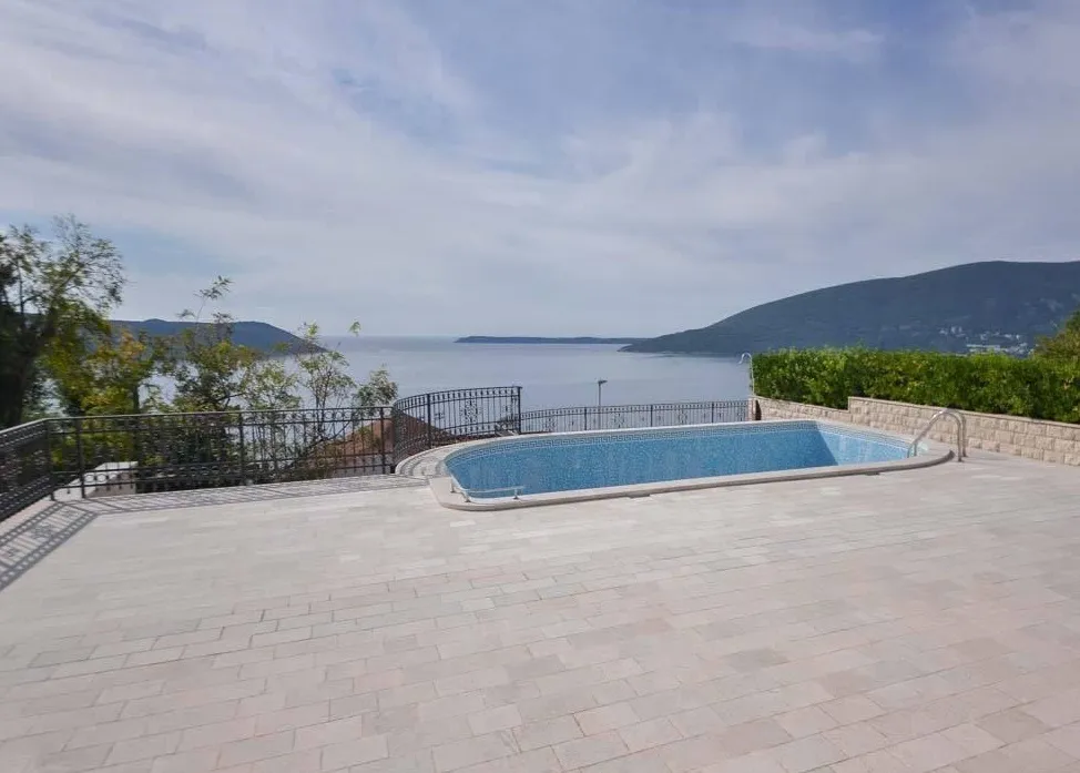 Outdoor swimming pool with blue tiles on a stone patio overlooking the sea and mountains.