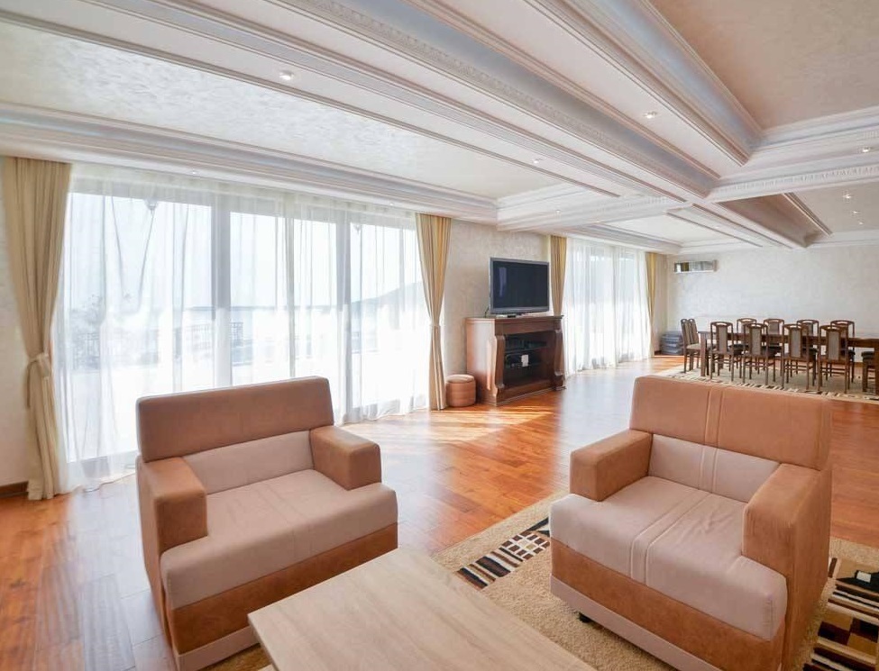 Living room with two beige sofas, a TV on a stand, and a dining area visible in the background.