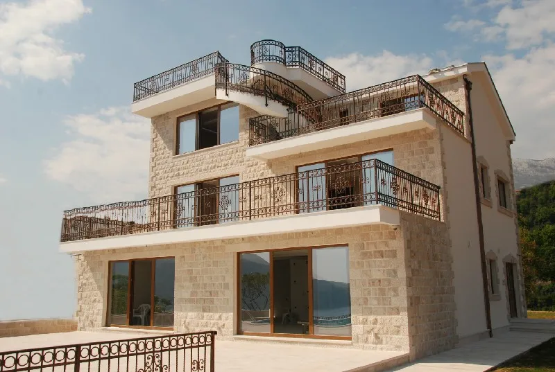 Exterior view of a multi-story stone house with balconies and wrought iron railings against the sky.