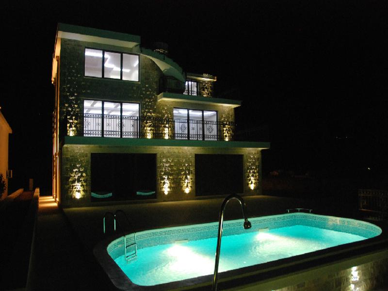 Three-story villa with a pool and nighttime facade lighting in Herceg Novi, Montenegro. Modern house with terraces.