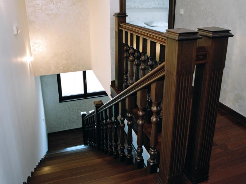 Wooden staircase with carved railings in the interior of a villa in Herceg Novi, Montenegro, with a view of the second floor.