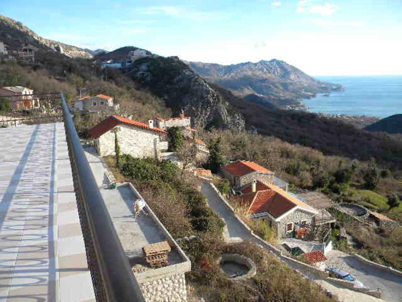 View from the house terrace in Budva, Montenegro: a panorama of mountains, stone villas with tiled roofs, and the sea bay.
