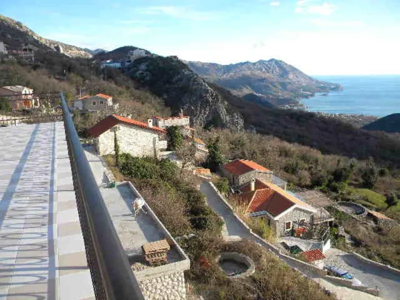 View from a tiled balcony overlooking mountainous terrain, stone houses, and the sea.