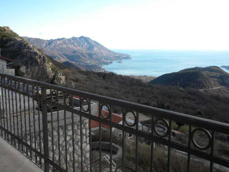 Panoramic view of the sea and mountains from the balcony of a house in Budva, Montenegro, with wrought-iron railing and stone facade finish.