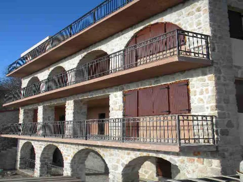 Stone building facade featuring arched openings, wooden shutters, and wrought iron balconies under a clear blue sky.
