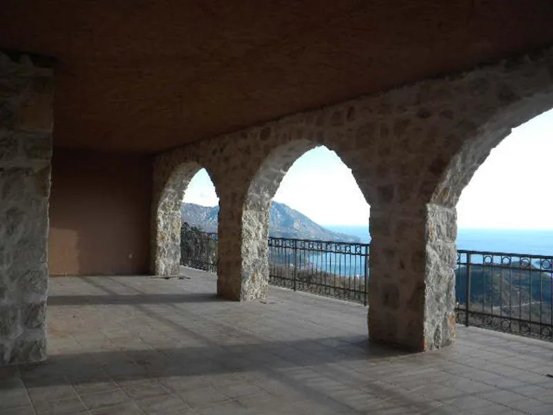 Stone arched terrace overlooking sea and mountains, tiled floor with wrought iron railings.