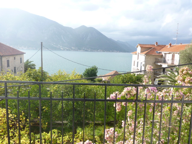 View from the balcony of a house in Kumbor, Montenegro: a panorama of the Bay of Kotor, mountains, and a blooming garden from the terrace.