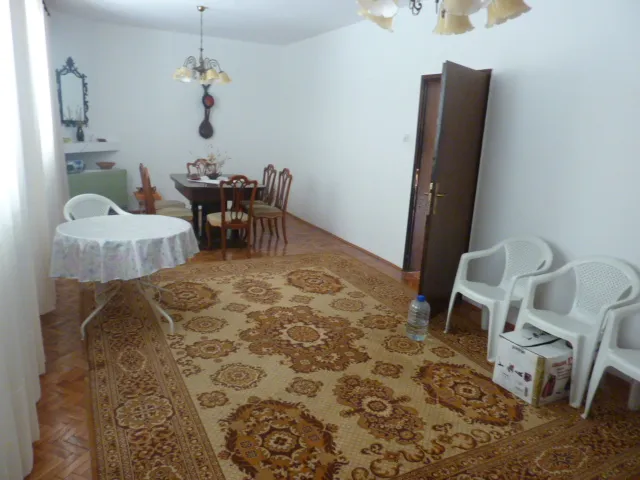 Living room with patterned rug, dining table, and white plastic chairs.