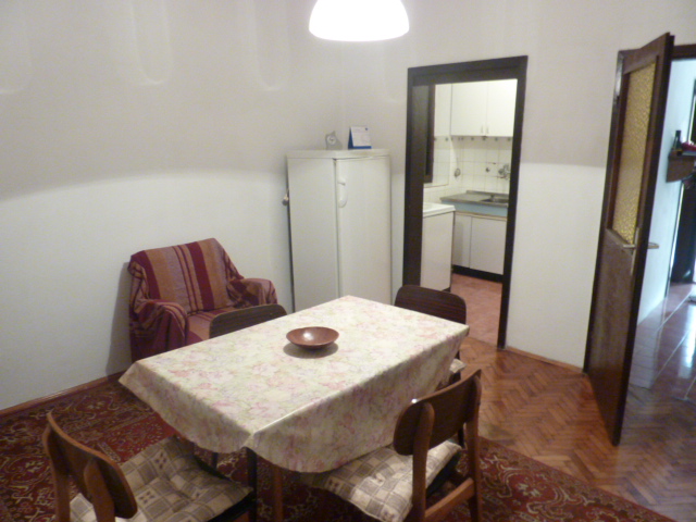 Living room with dining area in a house, Kumbor, Montenegro: wooden floor, table, chairs, and view of the kitchen.