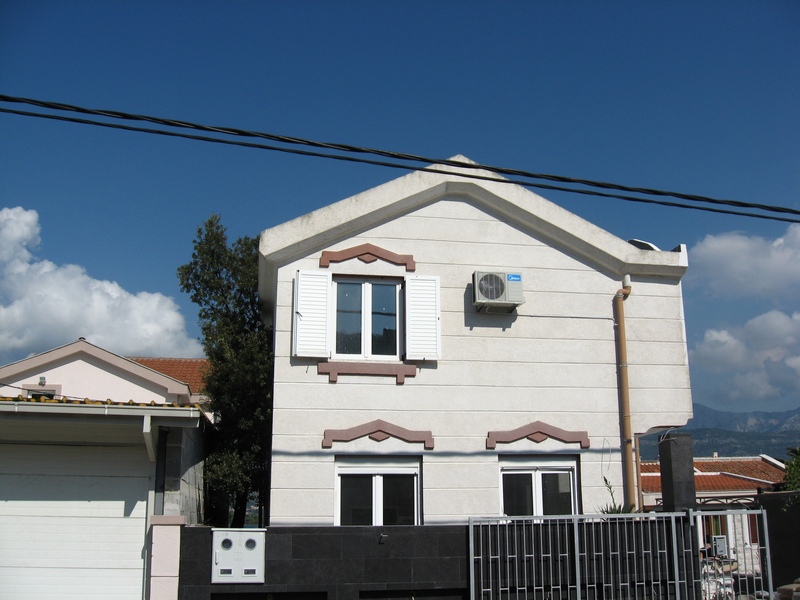 Two-story house in Tivat, Montenegro: light facade, white window shutters, air conditioner, and a modern fence.
