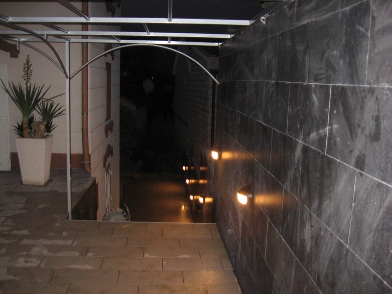 Evening terrace of a house in Tivat, Montenegro, with decorative wall lighting and modern-style floor tiles.