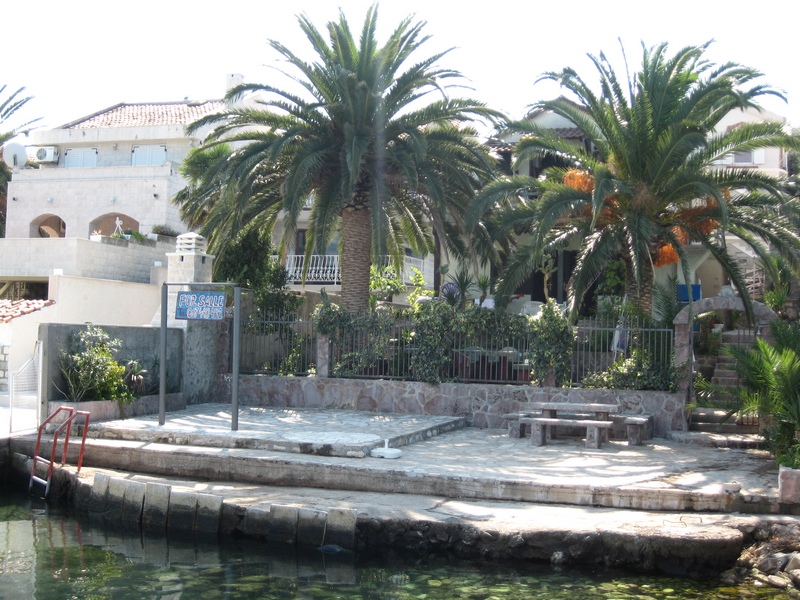 Two-story house in Tivat, Montenegro, with a private pier, stone terrace, palm trees, and sea access.