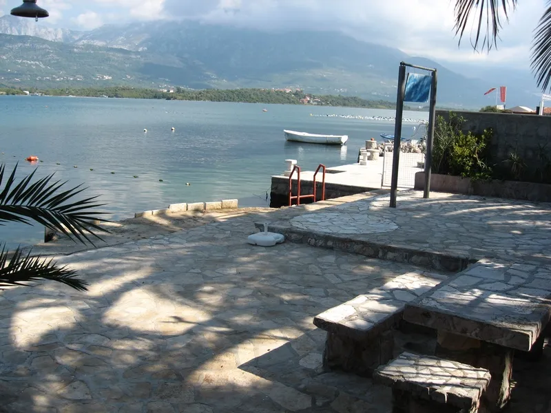 Stone terrace by the water with stone benches, view of the sea and mountains, boat at the dock.