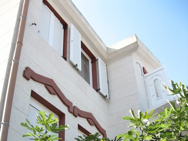 House facade in Tivat, Montenegro: light finish, white window shutters, and decorative elements in Mediterranean style.