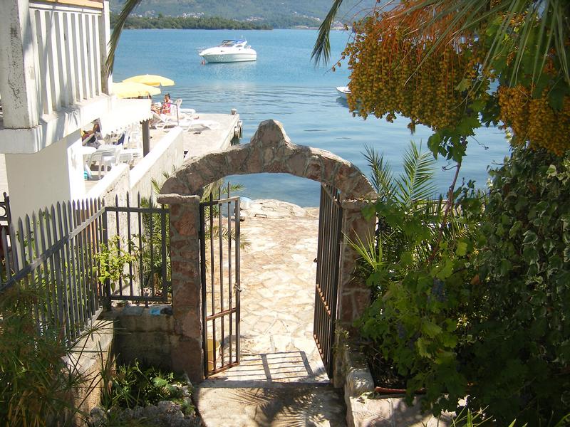 Stone arch with access to the sea and a private pier by the house in Tivat, Montenegro, with a view of a yacht and the bay.