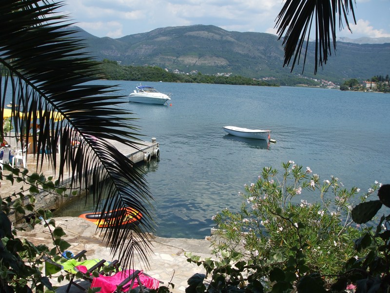 Sea view and pier from the private beach of a house in Tivat, Montenegro: palm trees, boats, and mountains in the background.
