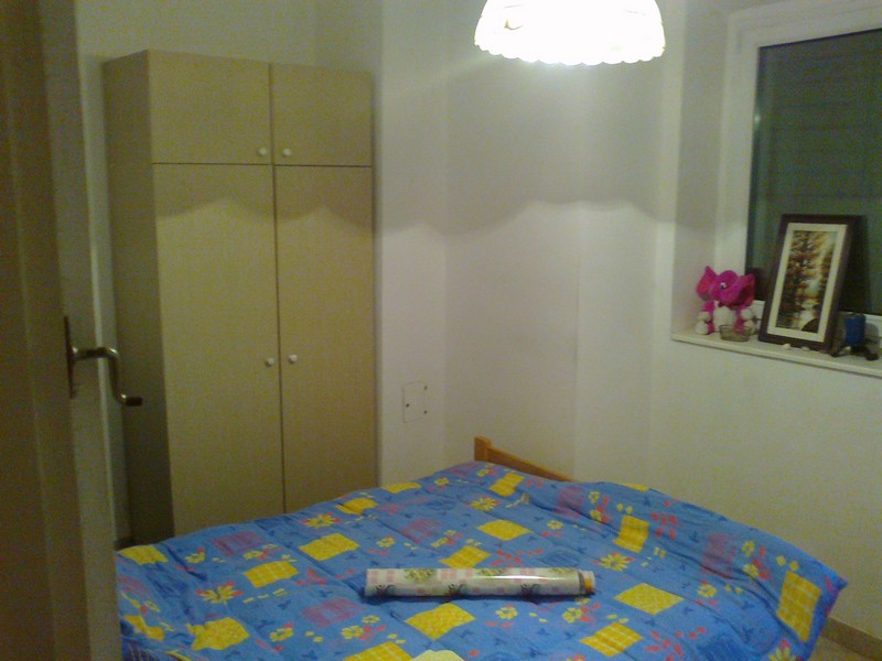 Cozy bedroom in an apartment in Budva, Montenegro: double bed, light-colored wardrobe, window with decor, and lamp.