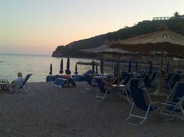 Beach scene with lounge chairs and umbrellas by the sea at sunset, sandy shore and cliffs.