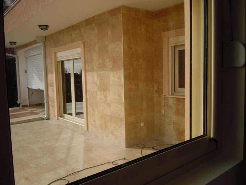 Spacious terrace with beige stone finishes in a house in Budva, Montenegro, view from the window of a balcony with roller shutters.