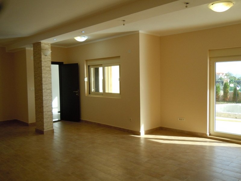 Spacious living room in a house in Budva, Montenegro: light finishes, tiled floor, decorative column, and access to the terrace.