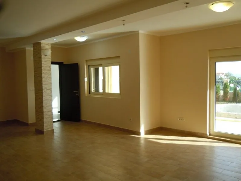 Empty room with beige walls, tiled floor, stone column, window, and glass door leading outside.