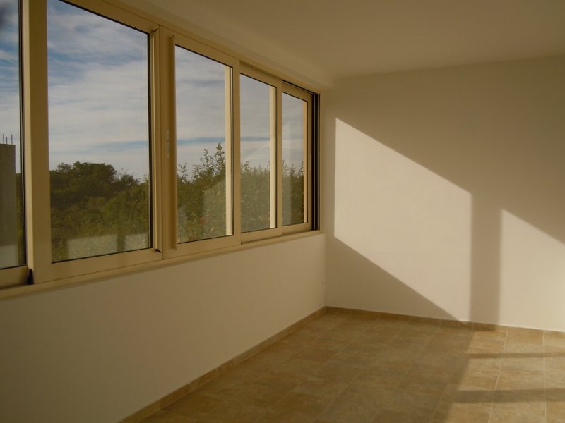 Bright balcony with panoramic windows and a view of greenery in a building in Budva, Montenegro. Tiled floor and white walls.