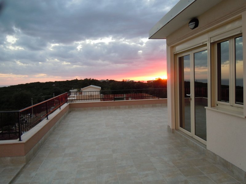 Spacious terrace with panoramic sunset views in a house, Budva, Montenegro: tiled flooring and access from the living room.
