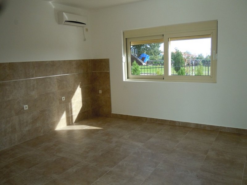 Bright kitchen in a house in Budva, Montenegro: tiled floor, tile backsplash, air conditioner, and a view of the green garden.