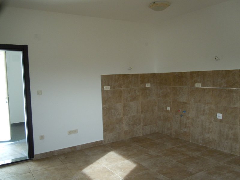 Bright kitchen in a house in Budva, Montenegro: a space for installing cabinetry with beige tile and utility connections.