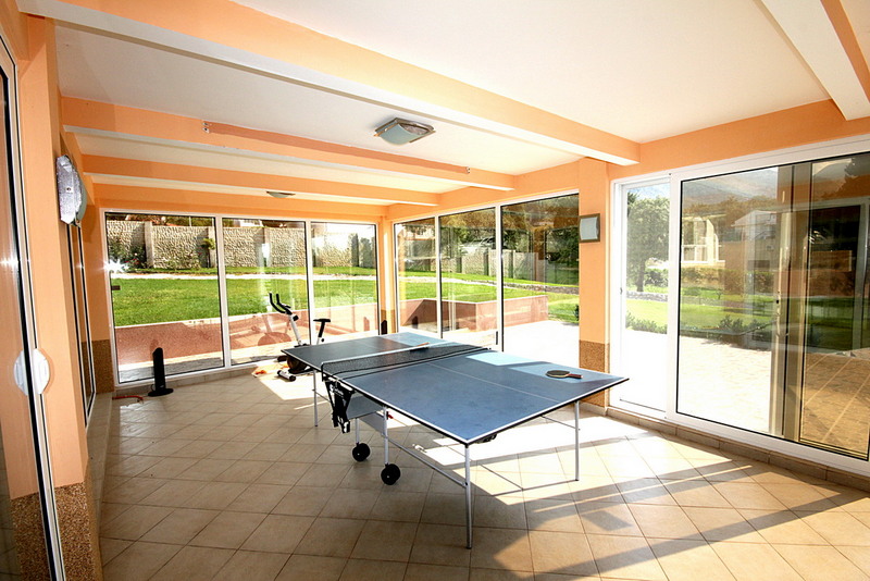 Game room with a ping-pong table and exercise machine in a house in Sutomore, Montenegro, with panoramic windows and a view of the garden.