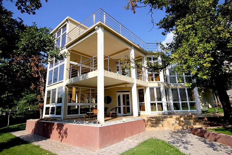 Modern three-story villa with panoramic windows and terraces in Sutomore, Montenegro, surrounded by a green garden.