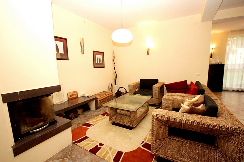 Living room with a fireplace and wicker furniture in a house, Sutomore, Montenegro. Cozy interior with a rug and a glass table.