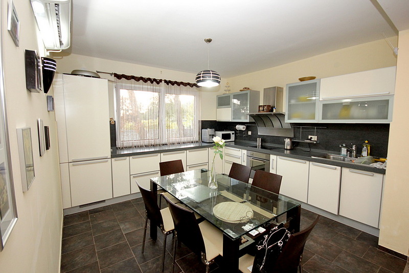 Modern kitchen with a glass table in a house for sale in Sutomore, Montenegro: light cabinetry and dark tile.