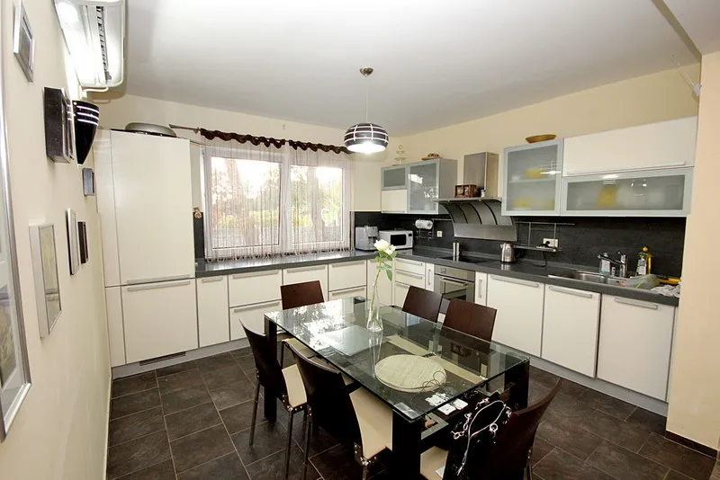 Modern kitchen with white cabinets, black countertops, refrigerator, and a glass dining table with chairs.