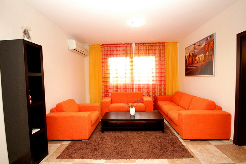 Living room with bright orange upholstered furniture in a house in Sutomore, Montenegro: a black coffee table and a rug on the floor.